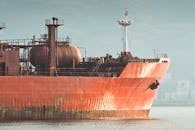 A close-up view of a large rusty industrial ship docked near a coastal city.