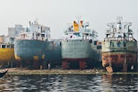 Row of large cargo ships docked at an industrial shipyard by the water.